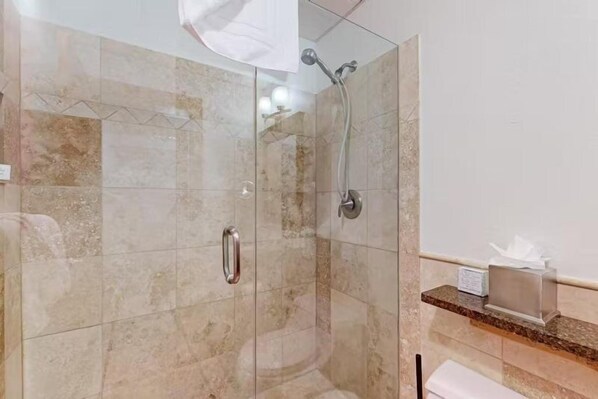 A glass-enclosed shower with a handheld showerhead and a wall-mounted faucet.