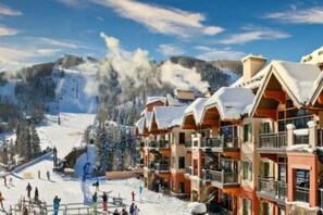 A ski resort with multi-story buildings, ski slopes, and a snowy mountain backdrop.
