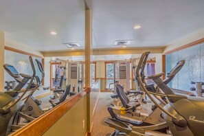 Ein Fitnessraum mit verschiedenen Trainingsgeräten, großen Fenstern und einer Spiegelwand.