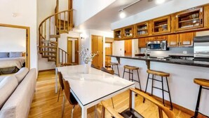 A modern kitchen with wooden cabinets, a central island with stools, and a staircase leading to an upper level. - Chic Ski In, Ski Out 2 Bedroom Penthouse in Beaver Creek Village (Avon)