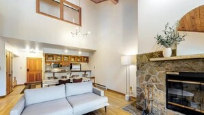 A modern living room with a sofa, a fireplace, and a kitchen in the background. - Chic Ski In, Ski Out 2 Bedroom Penthouse in Beaver Creek Village (Avon)
