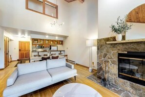 A modern living room with a sofa, a fireplace, and a kitchen in the background. - Chic Ski In, Ski Out 2 Bedroom Penthouse in Beaver Creek Village (Avon)