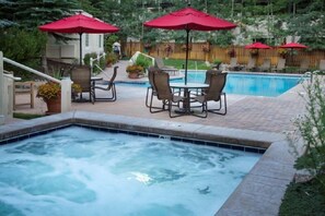 A hot tub with a pool, outdoor seating, and red umbrellas.