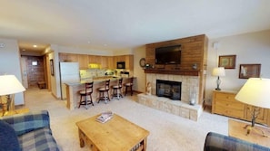 A spacious living room with a fireplace, a kitchen area with wooden cabinets, and a dining area with bar stools.