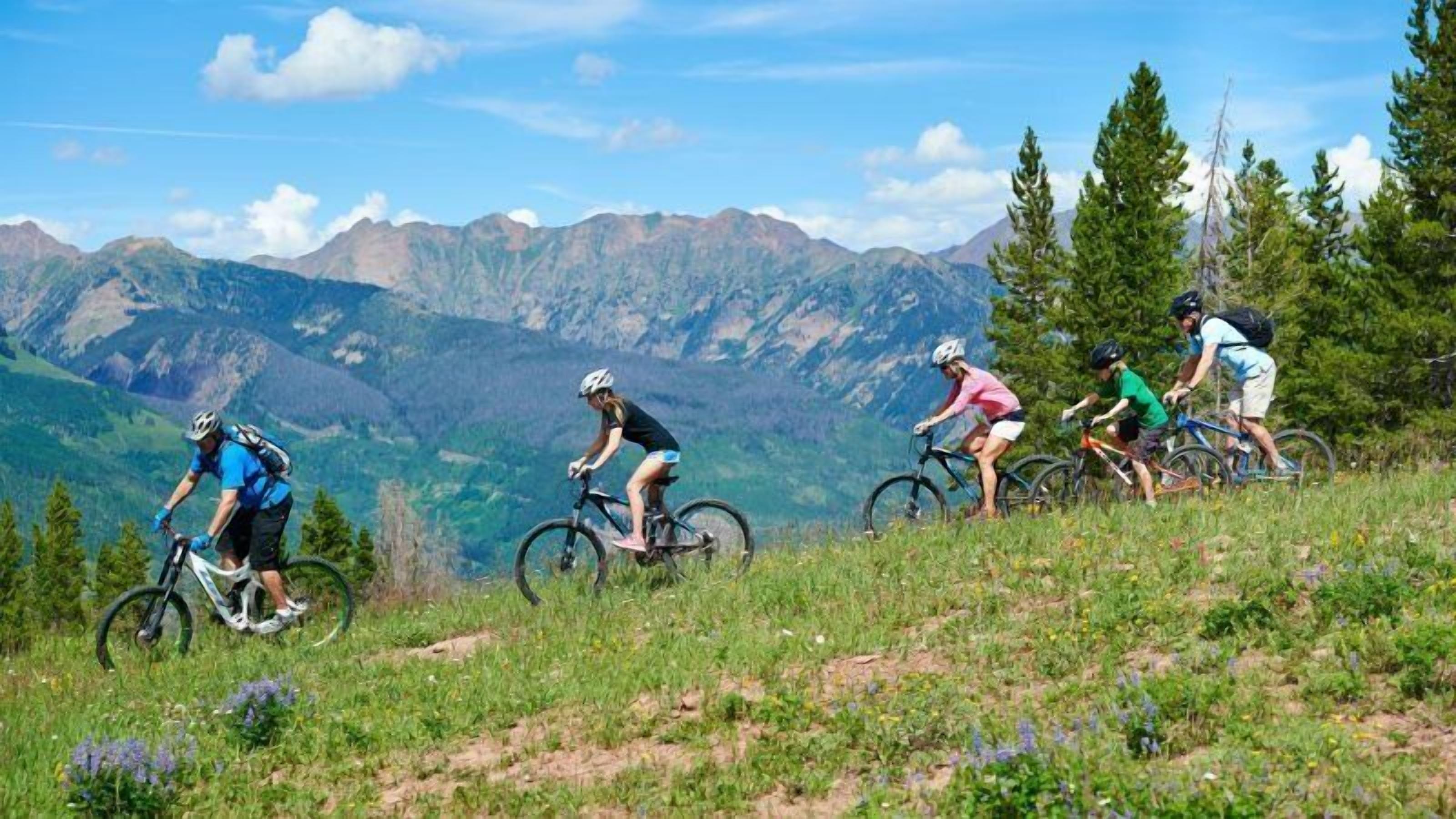 A group of cyclists on a mountain trail with a scenic mountain backdrop.