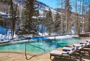Relax by the serene pool surrounded by snow-covered mountains and evergreen trees.