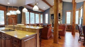 A spacious kitchen with a large island, wooden beams, and a stone fireplace.