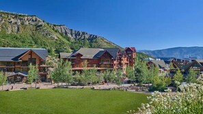 A lodge with multiple wooden buildings, a large lawn, and mountains in the background. - Luxury Ski in, Ski out 1 Bedroom Colorado Resort Vacation Rental in the Heart of Snowmass Base Village (Snowmass Village)