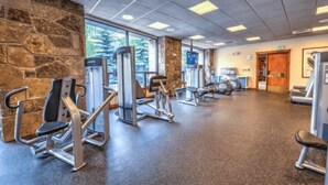 A gym with various exercise machines, stone walls, and large windows. - Downtown Breckenridge 2 Bedroom Condo - Steps to Lifts and Main Street (Breckenridge)
