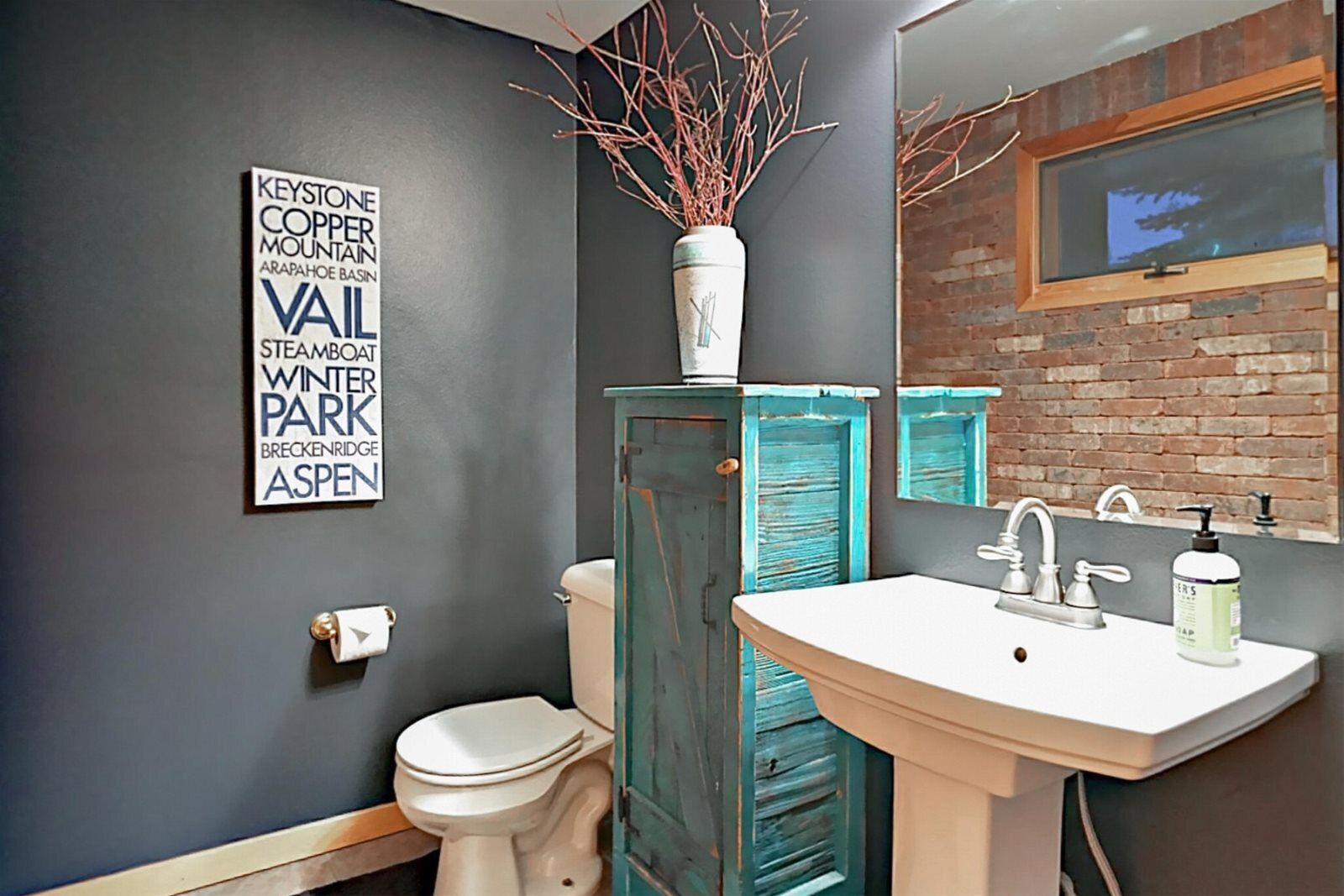 Un baño con un lavamanos blanco, un inodoro, un espejo y un letrero decorativo en la pared.