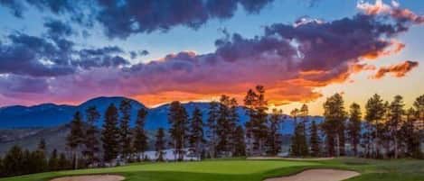 A golf course with a clear sky, mountains, and trees in the background.