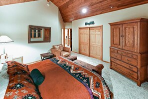 Une chambre avec un grand lit, une armoire en bois, une commode, un miroir et une porte donnant sur une autre pièce.