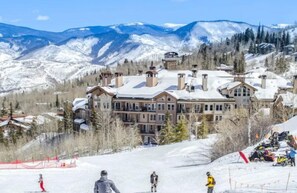 Ein Skigebiet mit einem großen Berghotel, Skipisten und schneebedeckten Bergen im Hintergrund.