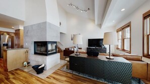 A modern living room with a fireplace, a sofa, a coffee table, and a TV. - Premier Ski in, Ski-out 3 Bedroom Condo With Spectacular Views, Heated Outdoor Pool and Hot Tub, Short Walk to Village (Snowmass Village)