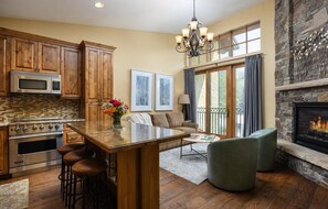 A kitchen with wooden cabinets, a central island, and a stone fireplace. - Luxury 3 Bedroom Lionshead Village Condo With Rooftop Pool, Hot Tubs (Vail)