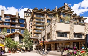 A multi-story hotel with stone facades, balconies, and a central entrance with a covered area. - Luxury 3 Bedroom Lionshead Village Condo With Rooftop Pool, Hot Tubs (Vail)