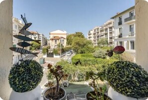 Een balkon met plantenbakken en uitzicht op een woonstraat met gebouwen en groen.