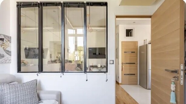 Un soggiorno moderno con un divano, un'ampia porta scorrevole in vetro e una zona cucina visibile attraverso la porta.
