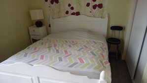 A neatly made bed with a patterned bedspread, a bedside table with a lamp, and a small stool. - La douceur de vivre (Blois)