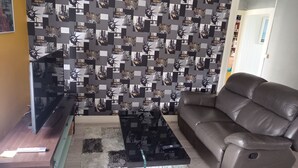 A living room with a patterned wallpaper, a leather sofa, a glass coffee table, and a flat-screen TV on a wooden stand. - La douceur de vivre (Blois)