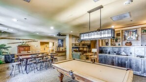 A pool table in a room with a high ceiling, wooden cabinets, and a variety of decorative items on the walls.
