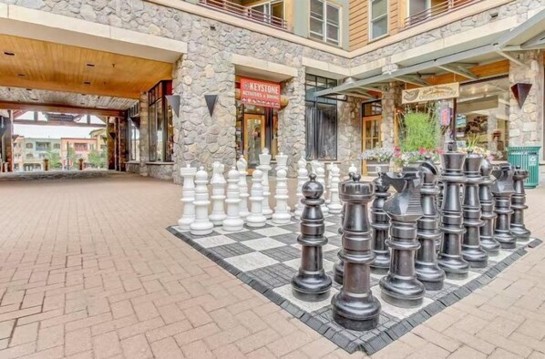 A large outdoor chessboard with a stone building in the background.