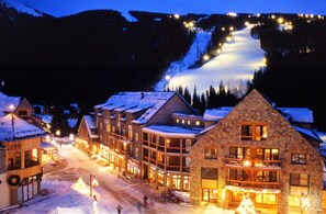 A snow-covered village with wooden buildings, a ski slope in the background, and a lit street. - River Run Village 1 Bedroom Renovated Condo at Silvermill Lodge (Keystone)
