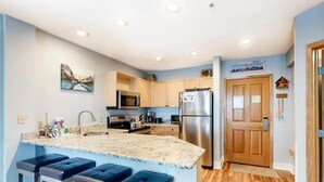 A modern kitchen with a granite countertop, stainless steel appliances, and wooden cabinets. There are three bar stools at the island.