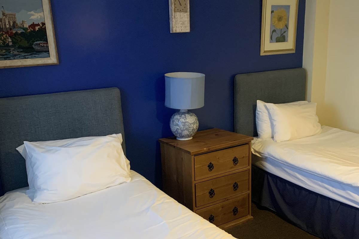 Una camera d'albergo con due letti singoli, un comodino in legno con una lampada e un quadro appeso al muro.