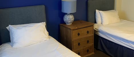 A hotel room with two single beds, a wooden nightstand with a lamp, and a framed picture on the wall.