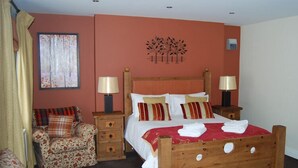 A bedroom with a wooden bed, two bedside tables with lamps, a floral armchair, and a painting on the wall. - The Barrington Arms Hotel (Swindon)