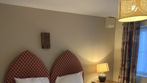 A neatly made bed with white linens and red polka dot headboards, a bedside lamp, and a window with floral curtains. - The Barrington Arms Hotel (Swindon)