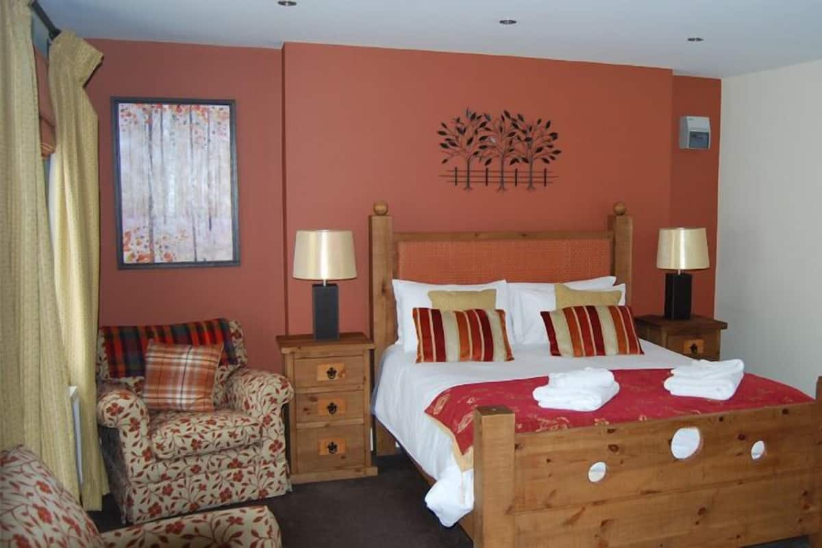 Una camera d'albergo con un letto in legno, due comodini con lampade, una poltrona con motivi floreali e un quadro appeso al muro.