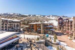 A ski resort with modern buildings, outdoor seating, and a view of snow-covered mountains. - Luxury Ski in, Ski out 2 Bedroom Colorado Resort Vacation Rental in the Heart of Snowmass Base Village (Snowmass Village)