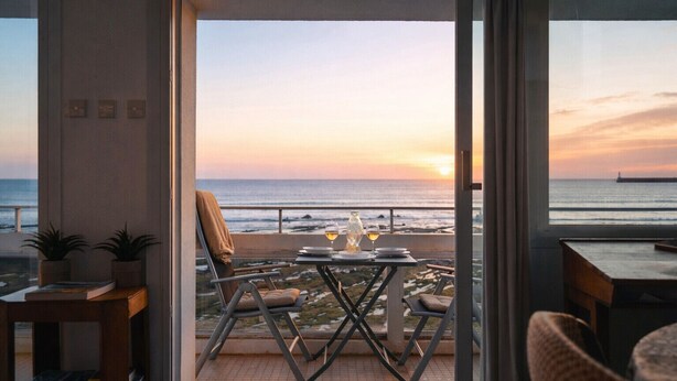 Ein Balkon mit einem Tisch für zwei Personen, der Blick auf einen Sonnenuntergang über dem Meer bietet.