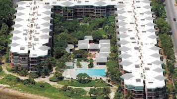 Un hôtel doté d’une piscine centrale, entouré d’une végétation luxuriante et donnant sur une plage.