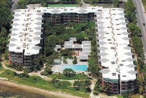 Un hotel con piscina central, rodeado de vegetación exuberante y una playa.