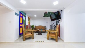 A room with a sofa, two wooden chairs, a TV mounted on the wall, and colorful artwork on the wall. - Ayenda Fundadores 1906 (Armenia)