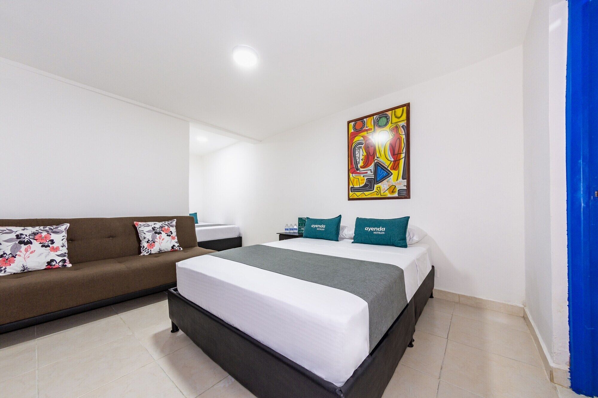 A hotel room with a bed, a sofa, and a painting on the wall.