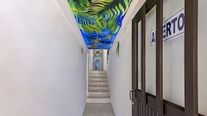 A hallway with a mural of a tropical scene on the ceiling, a staircase, and a door labeled "AERTO". - Ayenda Fundadores 1906 (Armenia)