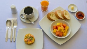 A breakfast setting with a plate of cubed fruit, toast, a muffin, a cup of coffee, a glass of orange juice, and a small bowl of jam. - Ayenda Fundadores 1906 (Armenia)