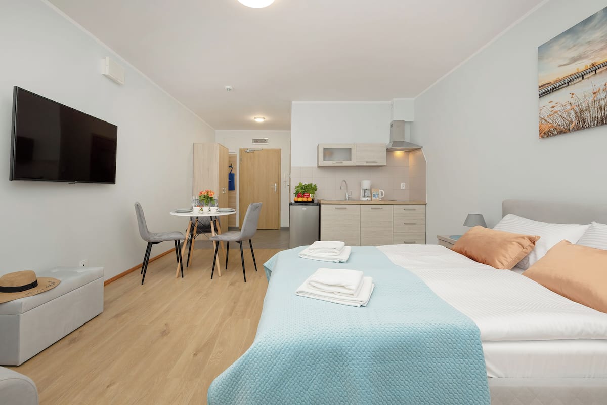 A modern hotel room with a bed, a TV, a desk, and a kitchenette.