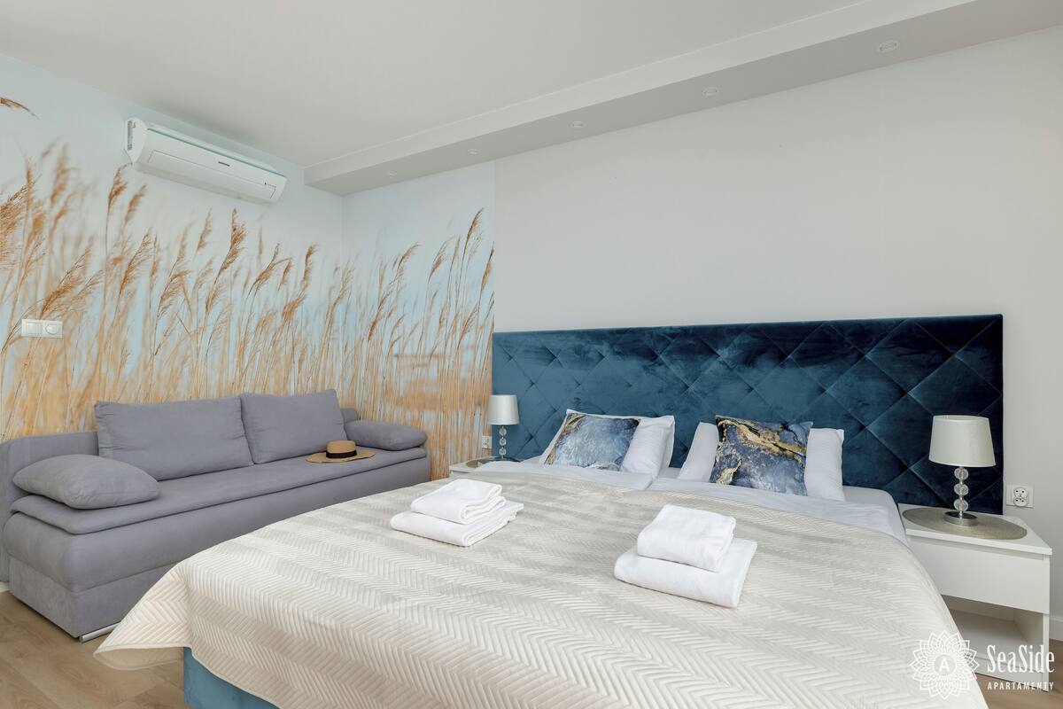 A modern bedroom with a large bed, a grey sofa, and a wall mural.