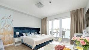 A modern hotel room with a large bed, a balcony with a table and chairs, and a dining area with a table set for two. - Seaside Apartamenty Kasprowicza (Kolobrzeg)