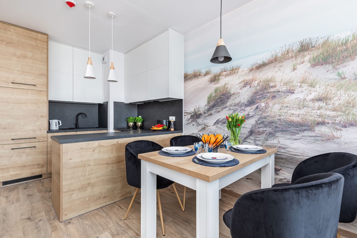 A modern kitchen with white cabinets, a wooden countertop, and black chairs.