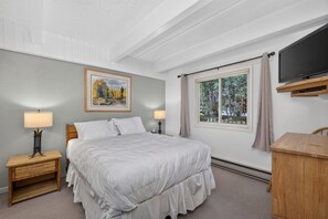 Une chambre d’hôtel avec un grand lit, deux tables de chevet, une télévision, une fenêtre avec des rideaux et un tableau au mur.