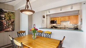 A dining area with a wooden table and chairs, a vase with flowers, and a kitchen in the background. - Lionshead 2-bedroom condo with pool (Vail)