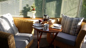 A cozy seating area with wicker furniture, a table set with plates, cups, and pastries, and a vase with flowers on a windowsill. - Cosy Stone Cottage - The Bungalow Perrotts Brook - Detached, parking, wifi. (Perrotts Brook Cirencester)