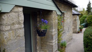 A stone building with a green door and a hanging flower pot. - Cosy Stone Cottage - The Bungalow Perrotts Brook - Detached, parking, wifi. (Perrotts Brook Cirencester)