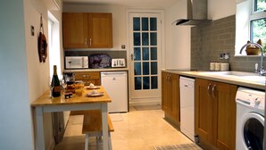 A compact kitchen with wooden cabinets, a microwave, a toaster, and a dishwasher. - Cosy Stone Cottage - The Bungalow Perrotts Brook - Detached, parking, wifi. (Perrotts Brook Cirencester)